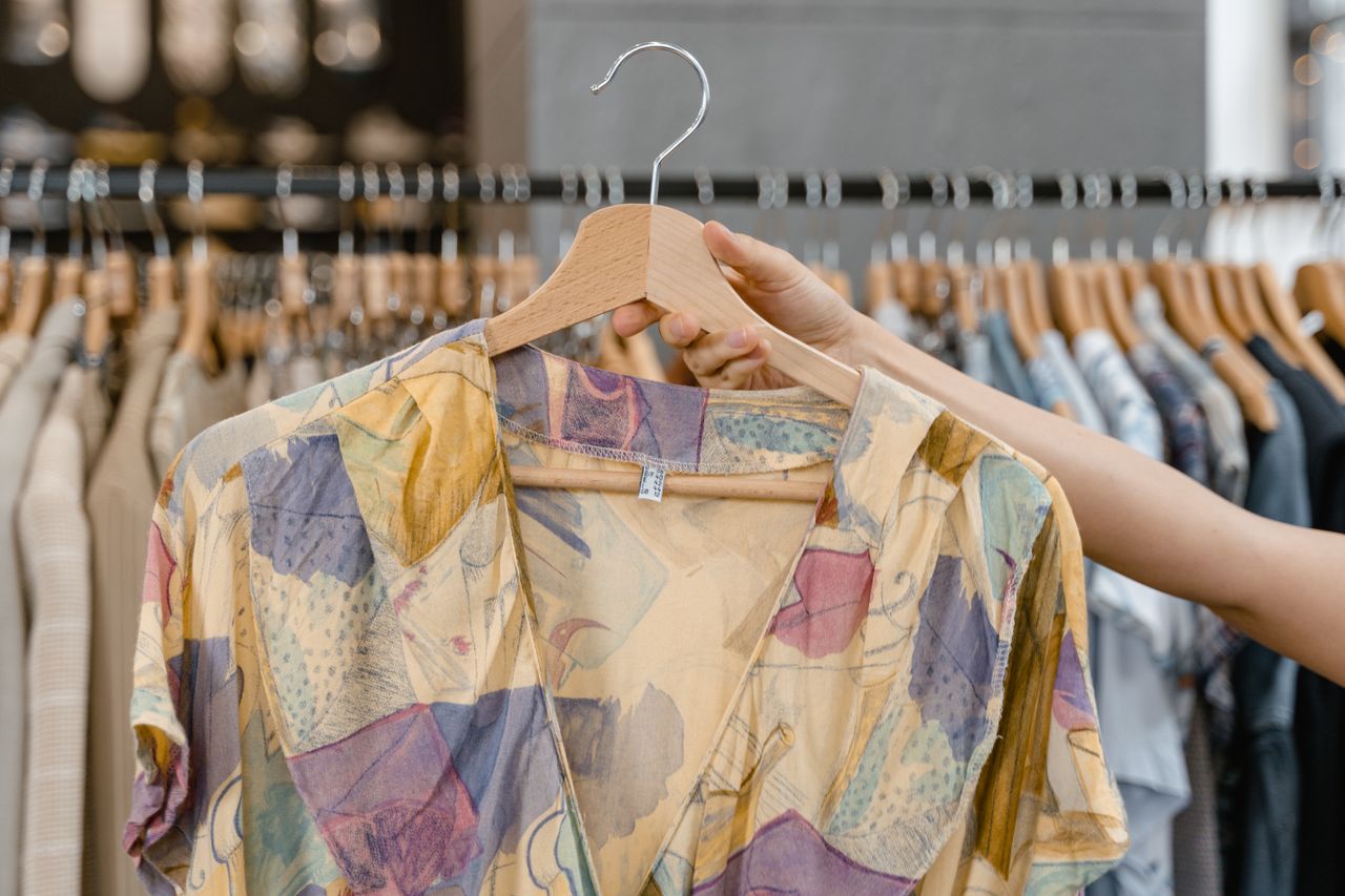 A person holding a vibrant patterned dress on a hanger inside a clothing store.